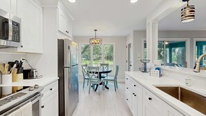 Una cocina moderna con armarios blancos, electrodomésticos de acero inoxidable y un comedor con mesa y sillas.