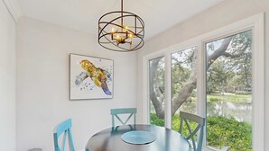 Un comedor con una mesa redonda, sillas color turquesa, un cubo de basura metálico y una araña.