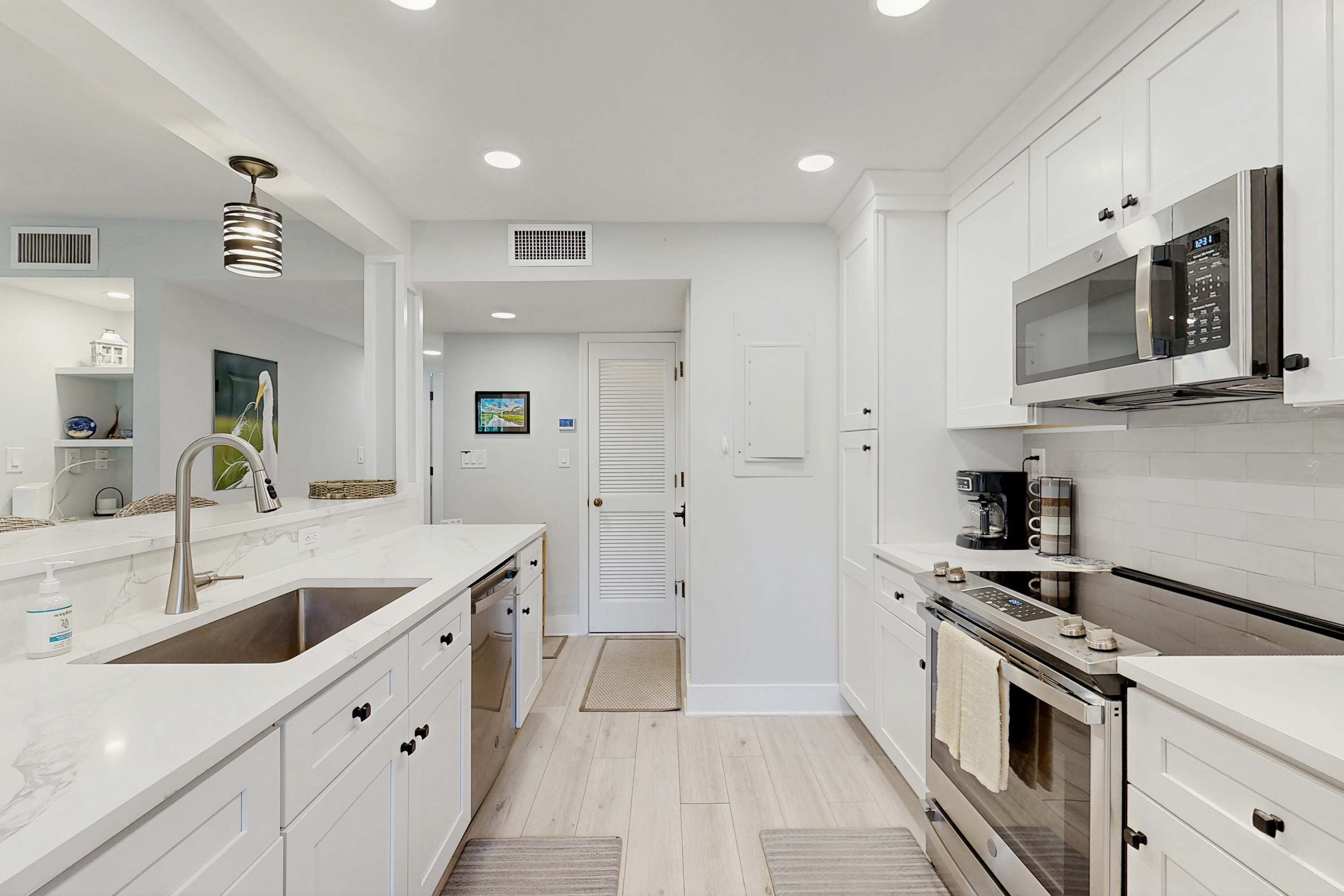 A modern kitchen with white cabinetry, stainless steel appliances, and a marble countertop.