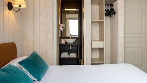 Habitación de hotel con cama, baño con lavabo y espejo, y armario con ropa colgada.