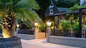 Entrada de un hotel con un cartel que dice "Hotel de la Plage", rodeada de abundante vegetación y un camino bien iluminado.