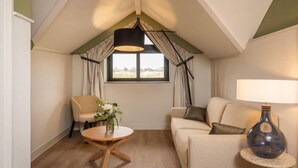 Una habitación acogedora con techo alto, una mesa redonda de madera con un jarrón de flores, un sofá beige y una lámpara sobre una mesita auxiliar.