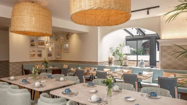 Un restaurante con varias mesas dispuestas para comer, con lámparas colgantes de mimbre y cuadros en las paredes.