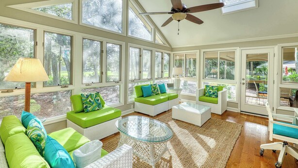 A sunlit room with large windows, a ceiling fan, and green and white furniture. - Remodeled Home with Deck, Sun Porch & In-Law Suite - Dogs OK, Beach Nearby (Kiawah Island)
