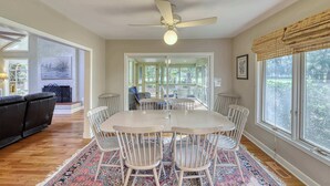 A spacious dining area with a white table and chairs, a ceiling fan, and large windows offering a view of the outdoors. - Remodeled Home with Deck, Sun Porch & In-Law Suite - Dogs OK, Beach Nearby (Kiawah Island)