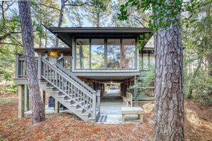 A modern cabin with a wooden deck, a staircase, and a bench.