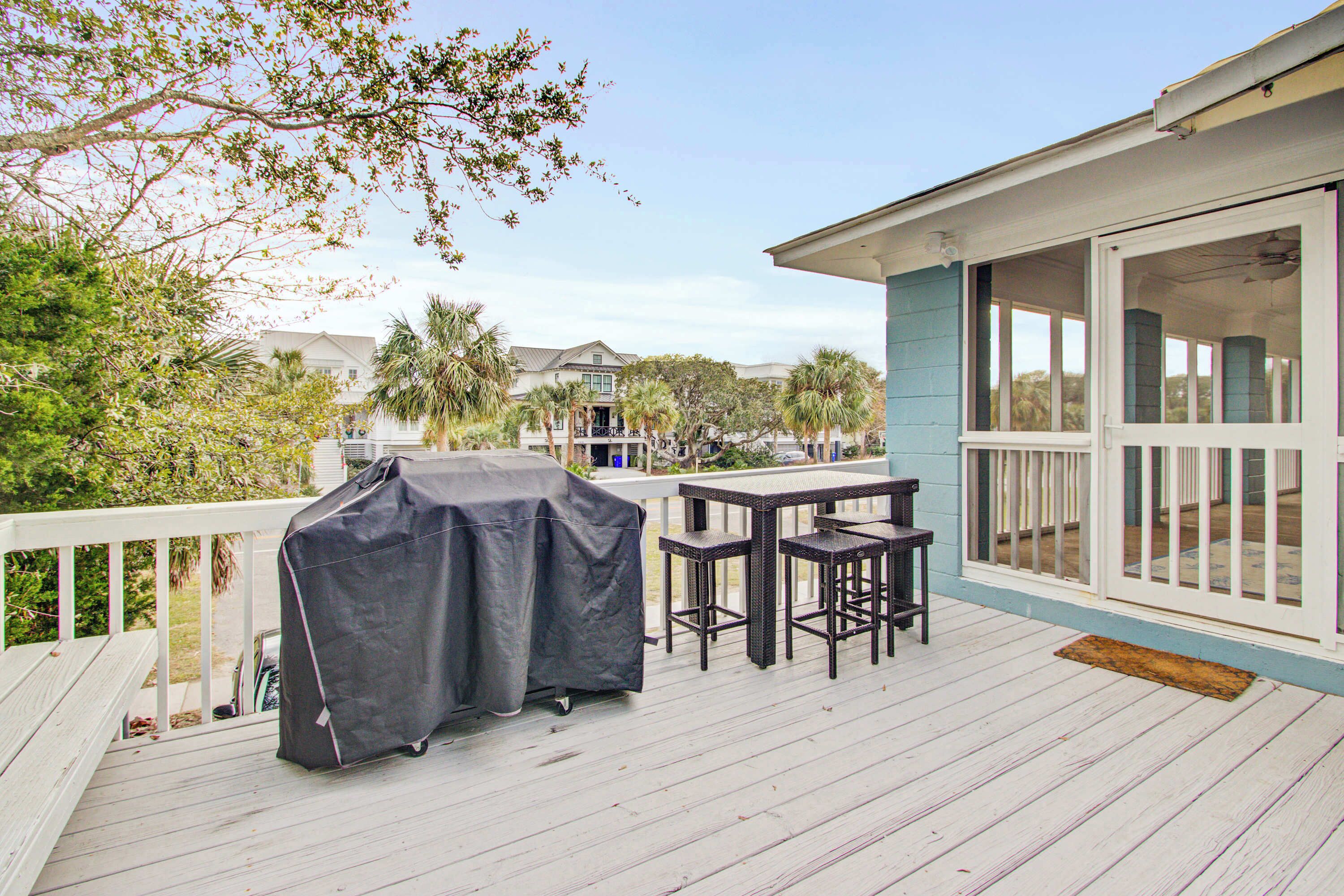 A covered outdoor deck with a grill, two bar stools, and a table.