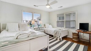Un dormitorio con dos camas, ventilador de techo, televisión y ventana con persianas.