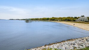 A waterfront property with a pier extending into calm waters, a sandy beach, and a large house with a green roof. - Stylish, Dog-Friendly, 30-Day Rental House w/Free WiFi, W/D, and Furnished Patio (Charleston)