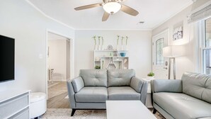 A modern living room with a grey leather sofa, a white coffee table, and a ceiling fan. - Stylish, Dog-Friendly, 30-Day Rental House w/Free WiFi, W/D, and Furnished Patio (Charleston)