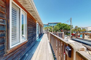 A wooden deck with a railing, a wooden building with large windows, and a clear blue sky. - Dog-Friendly, Downtown Folly Beach Condo w/Free WiFi, Flatscreen TVs & more (Folly Beach)