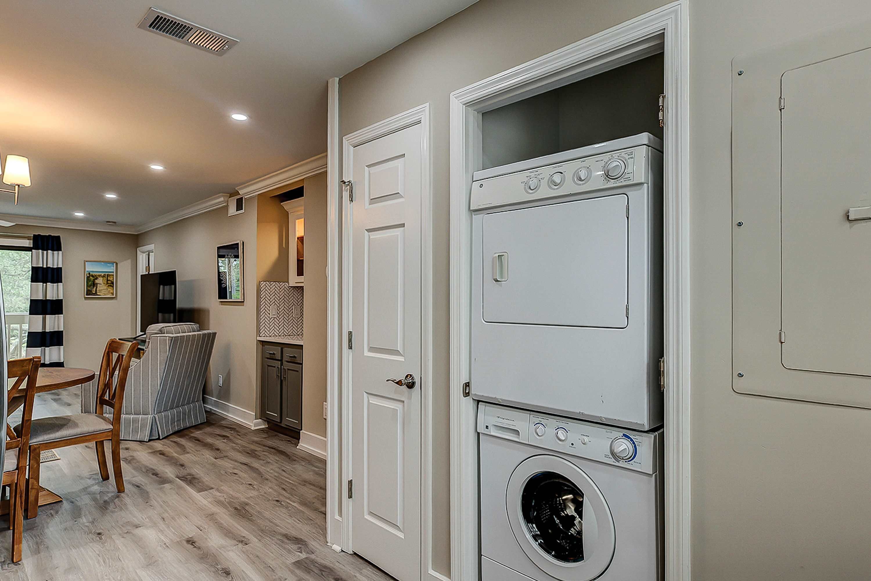 A laundry room with stacked washers and dryers, a dining area with chairs, and a kitchen in the background.