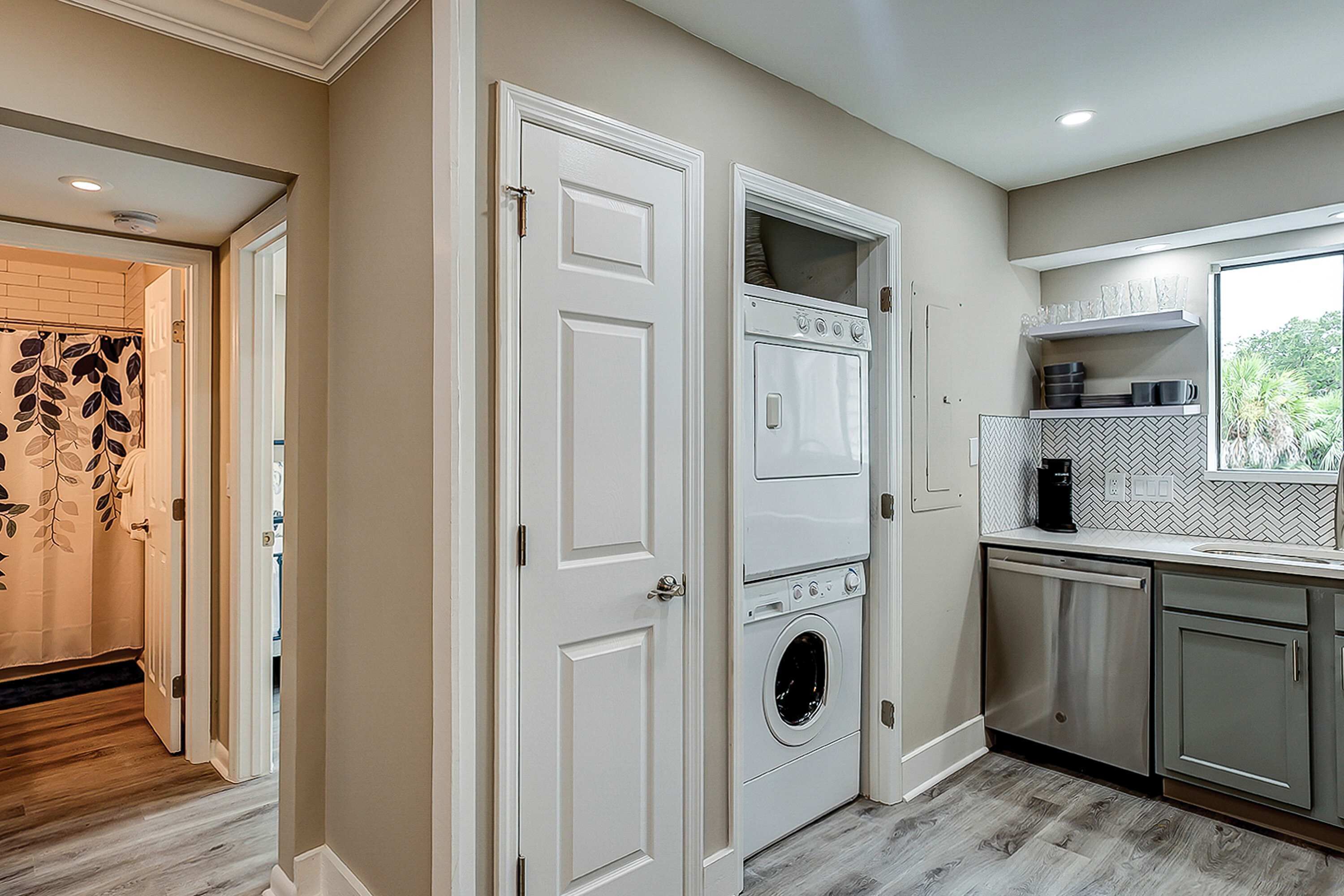 A laundry room with a washer and dryer, a window with a view of greenery, and a tiled backsplash.