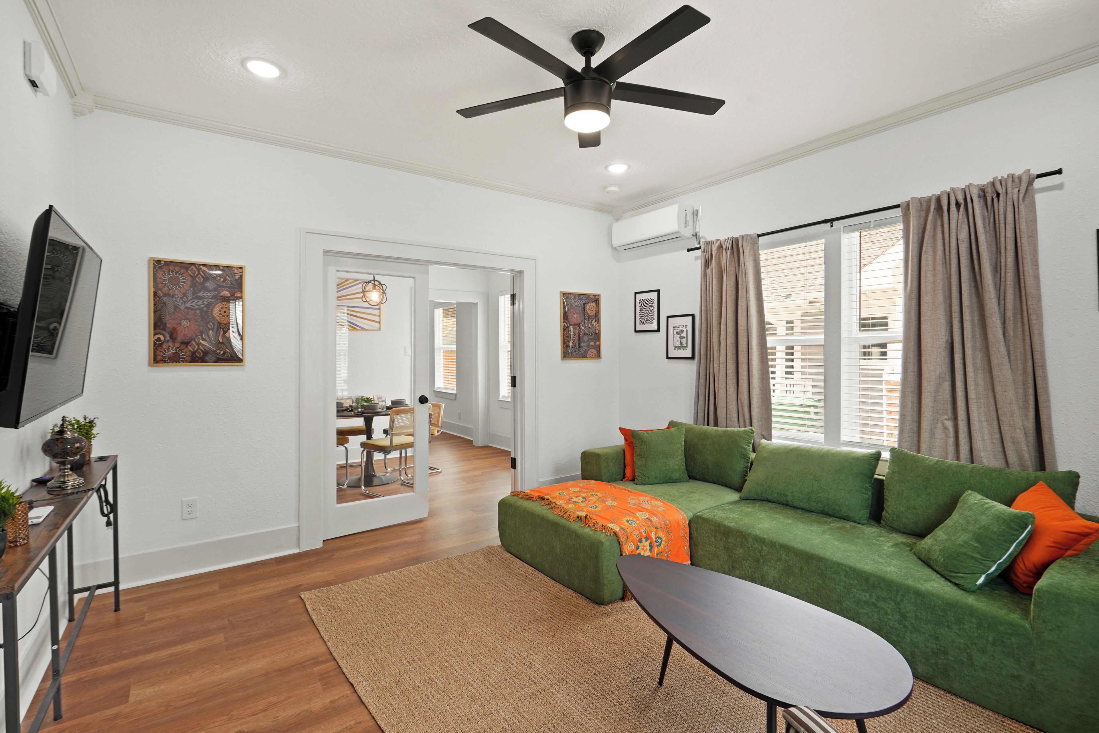 A modern living room with a green sofa, a small table, a ceiling fan, and a TV on a stand.
