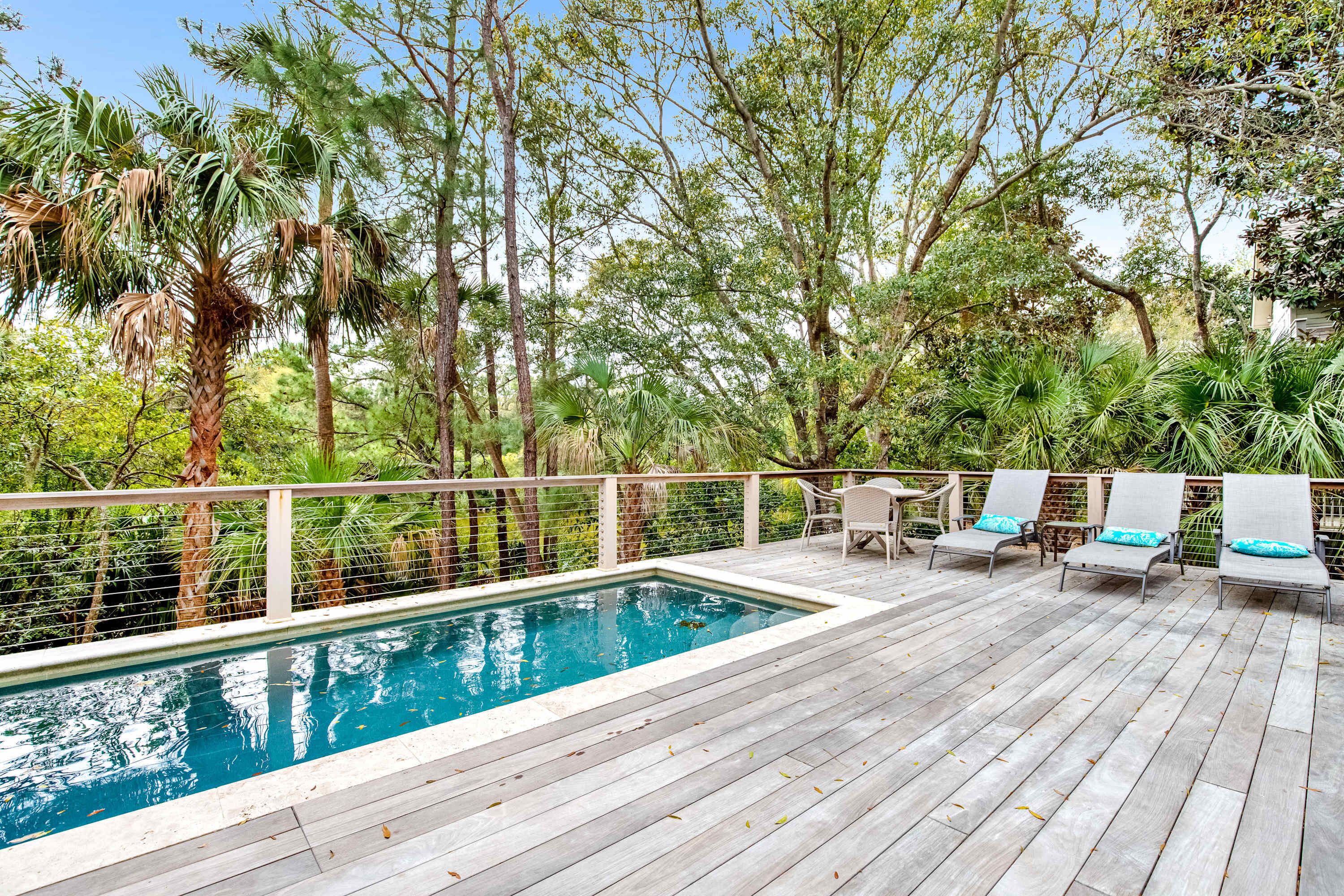 A wooden deck with a swimming pool, surrounded by lush greenery and trees.