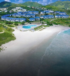 An aerial view of a coastal resort with multiple buildings, a sandy beach, and two swimming pools. - Serenity by the Sea - Beachfront studio in Mont Vernon (Cul-de-Sac)