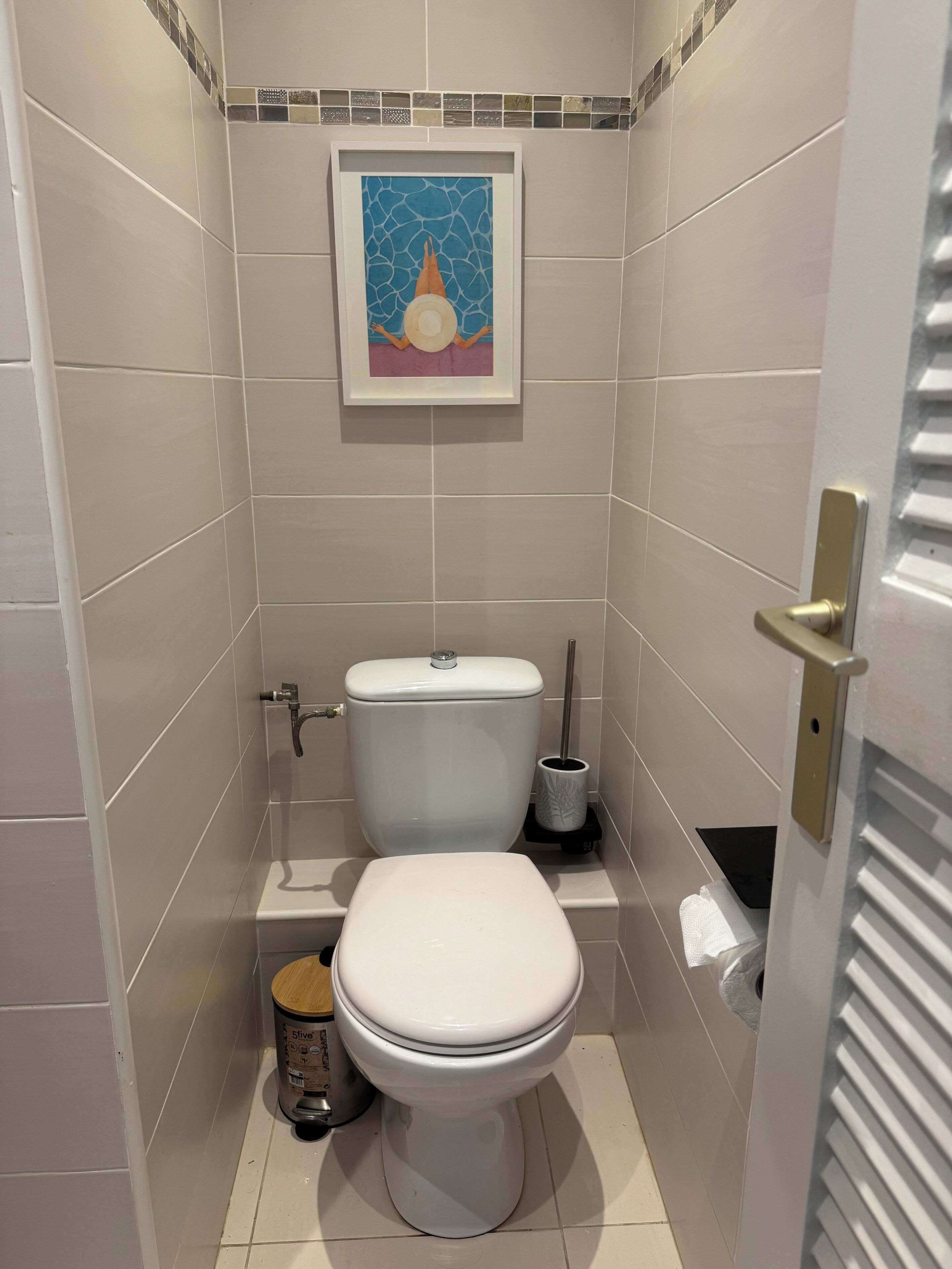 Un baño pequeño y moderno con inodoro, bidé y una obra de arte enmarcada en la pared.