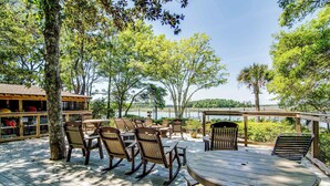 A wooden deck with outdoor seating, including chairs and a table, overlooking a body of water. - Dog-friendly home with deck, grill & pool - easy walk to beach, dining & shops (Kiawah Island)