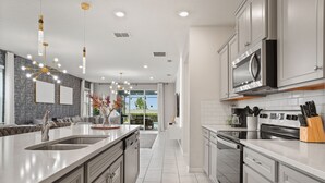 Una cocina moderna con una isla grande, electrodomésticos de acero inoxidable e iluminación colgante.