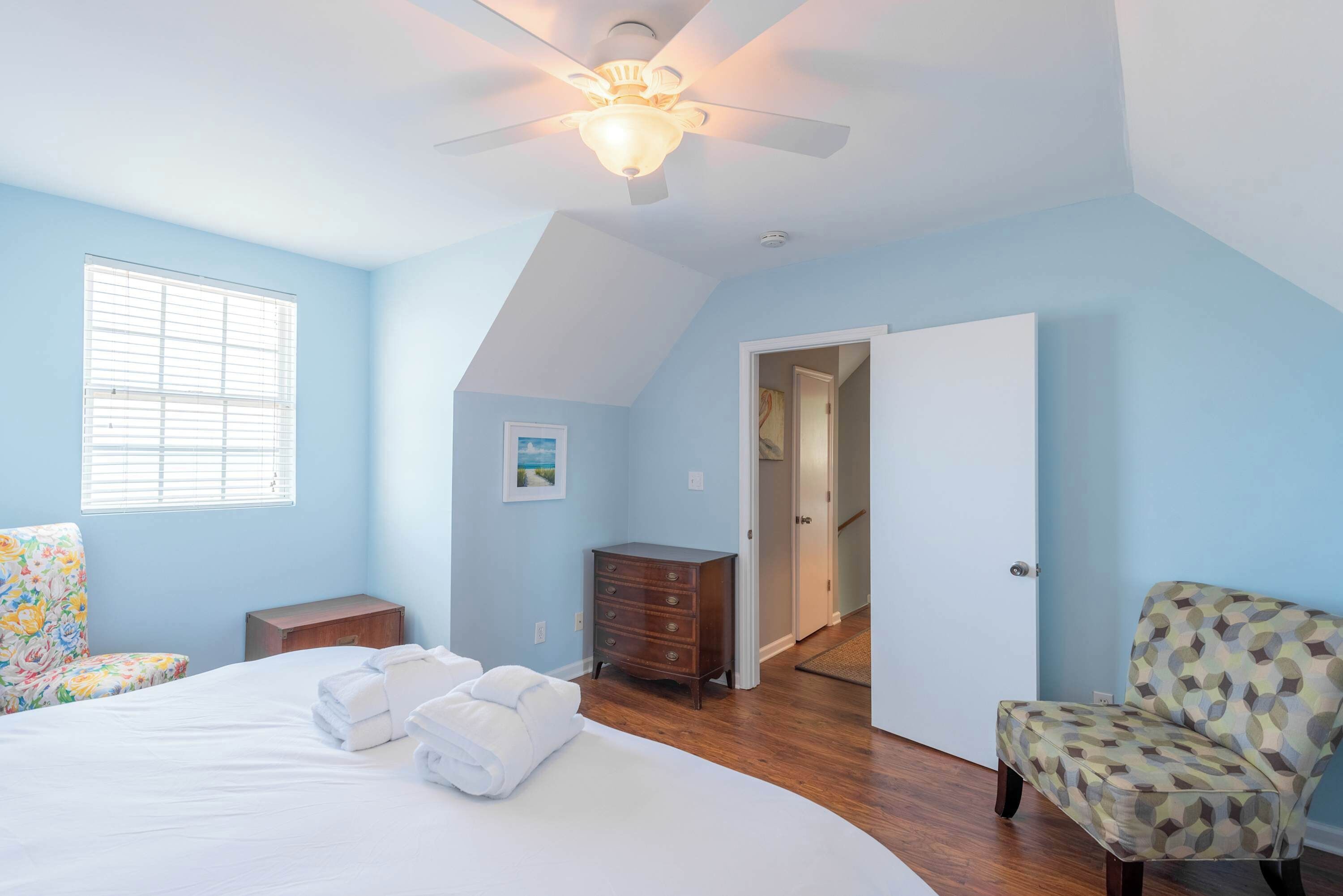 A bedroom with a bed, a dresser, a chair, and a ceiling fan.