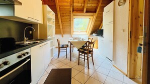 A kitchen with a stove, sink, and wooden ceiling beams. There is a dining table with chairs and a window above it.