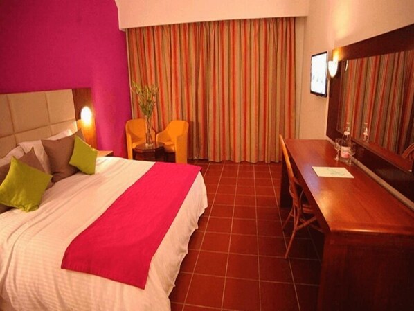 Une chambre d’hôtel avec un lit, un bureau, une chaise et une grande fenêtre avec des rideaux.