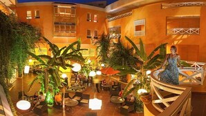 A courtyard with outdoor seating, palm trees, and a person on a balcony. - regency hammamet (Hammamet)