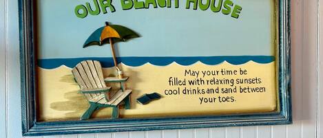A decorative sign with the text "OUR BEACH HOUSE" and a beach scene illustration.