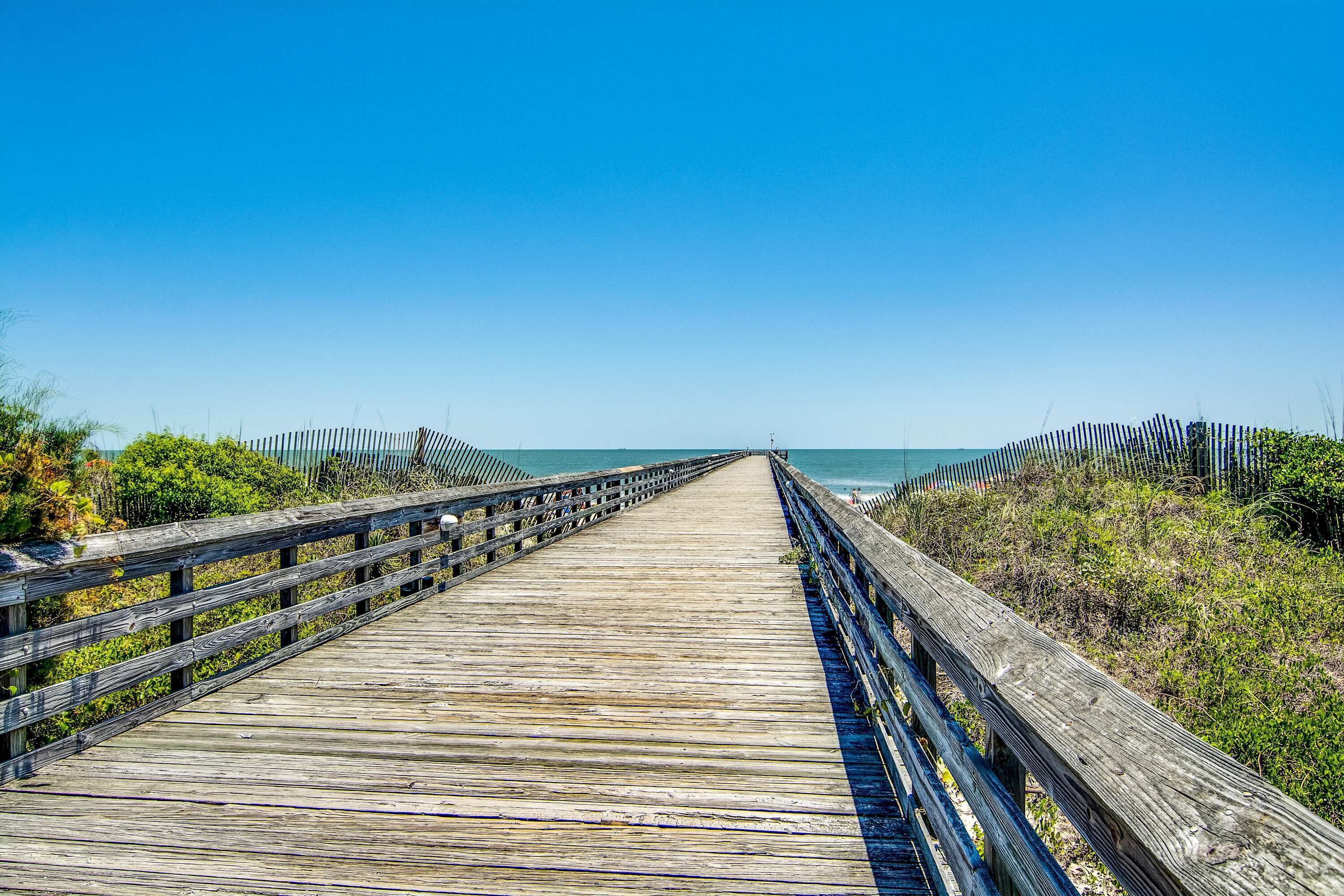 Un muelle de madera que conduce a la playa, con barandillas a ambos lados.