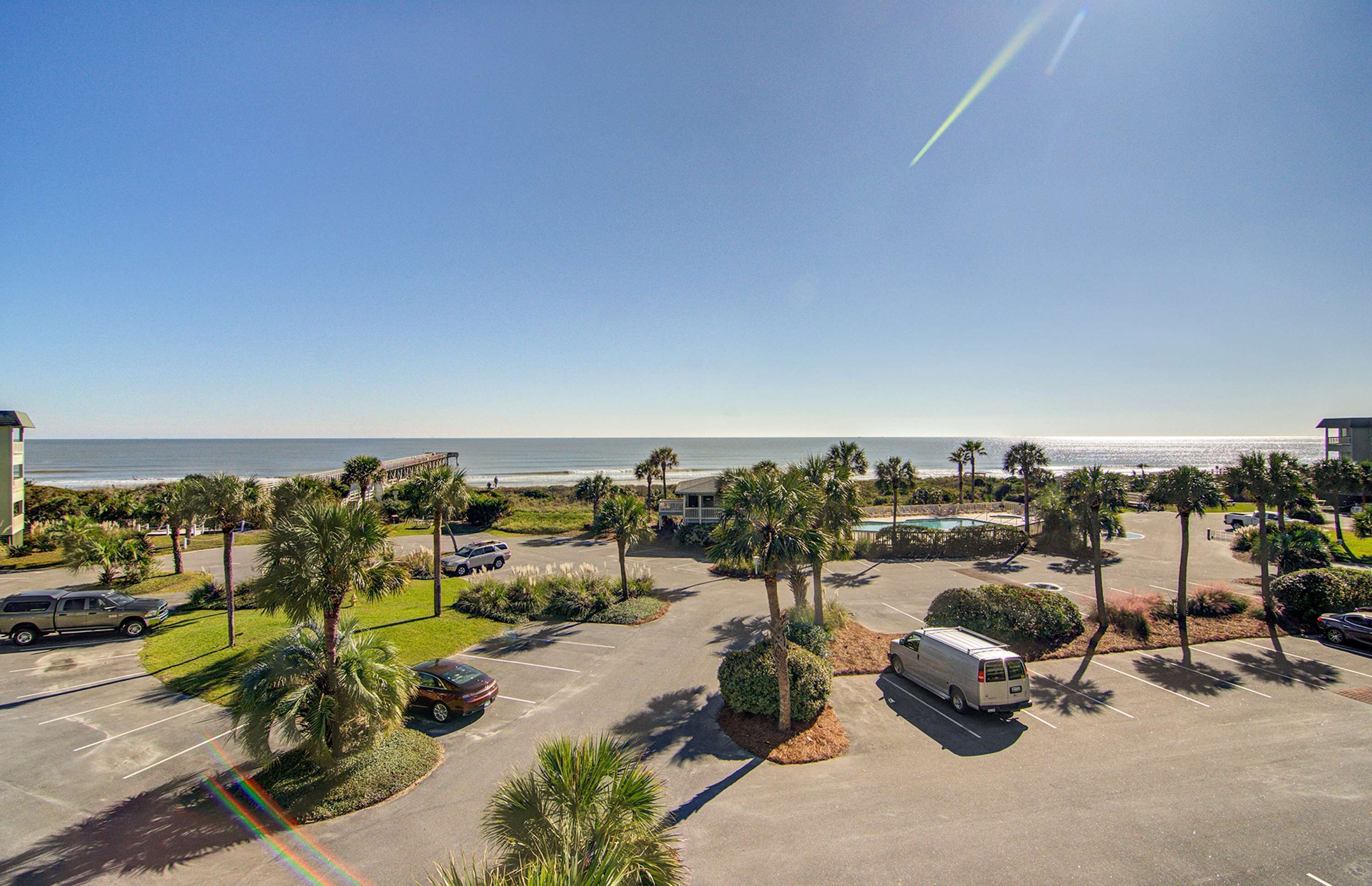 A parking lot with a view of the ocean, palm trees, and a building in the background.