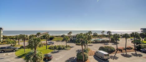 A parking lot with a view of the ocean, palm trees, and a building in the background.