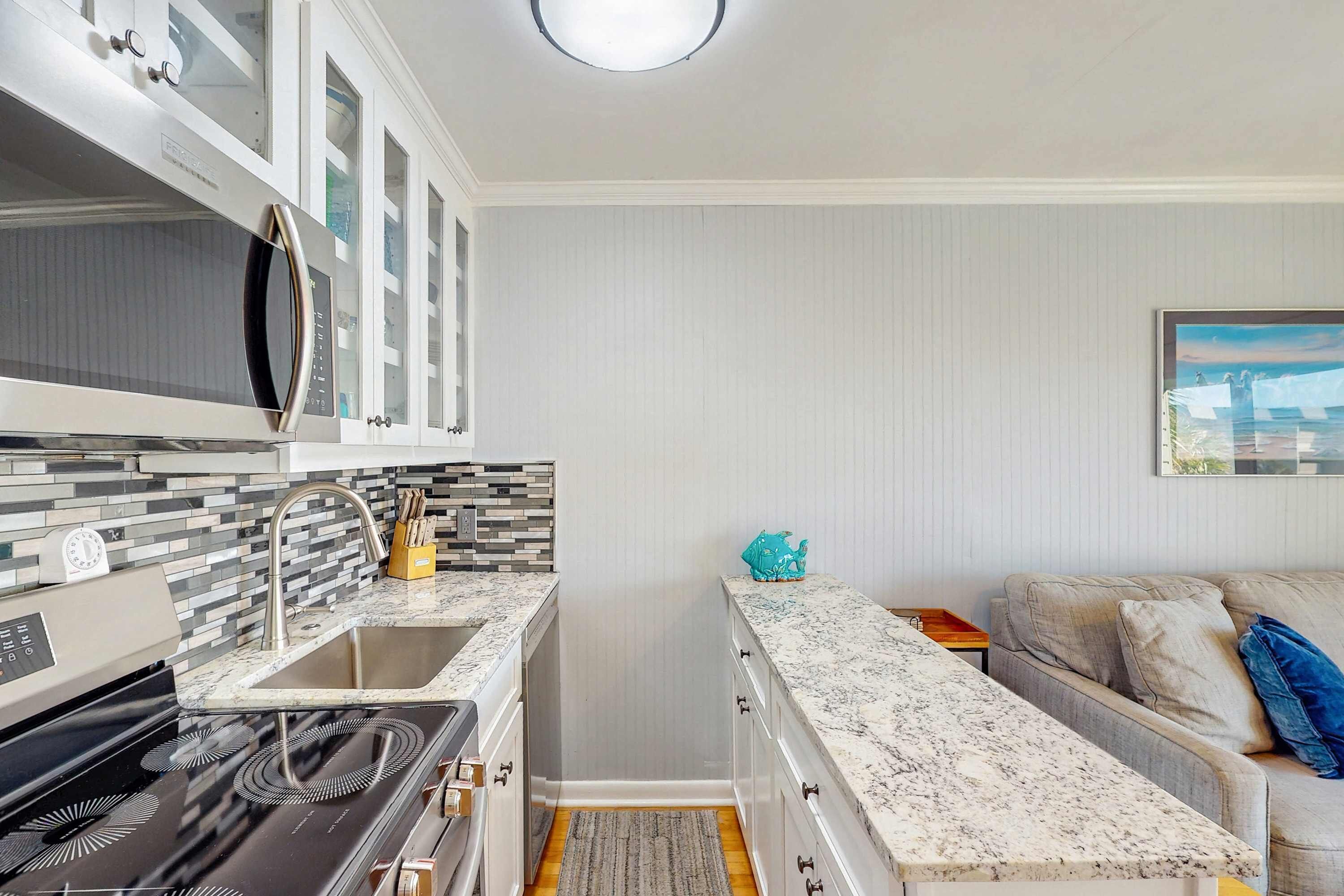 A compact kitchen with a stove, sink, and white cabinets.