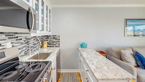 A compact kitchen with a stove, sink, and white cabinets. - Renovated villa with gorgeous ocean views, pool, grills, & great location (Isle of Palms)