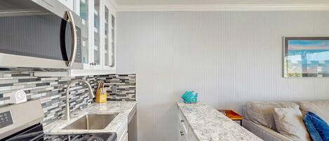 A compact kitchen with a stove, sink, and white cabinets.