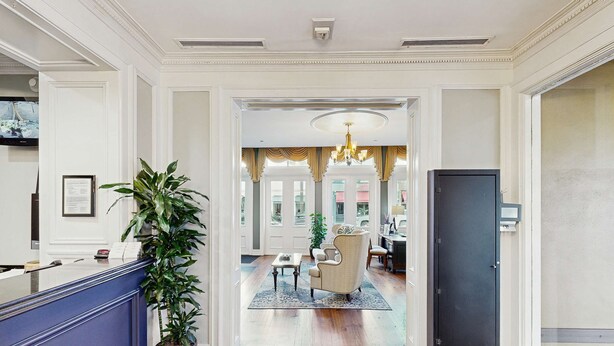 Un vestíbulo de hotel con mostrador de recepción, una planta en maceta, una araña y un área de comedor con sillas y una mesa.
