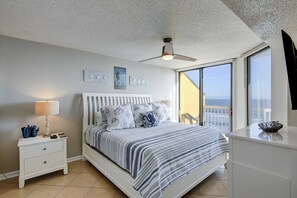 A bedroom with a bed, nightstand, lamp, and a view of the ocean through a large window. - Oceanfront villa with incredible views, balcony & 2 community pools (Folly Beach)