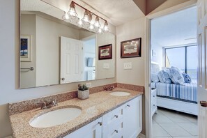 A bathroom with two sinks, a large mirror, and a vanity with drawers. There are framed pictures on the wall and a door leading to a bedroom. - Oceanfront villa with incredible views, balcony & 2 community pools (Folly Beach)