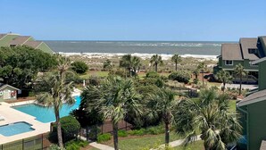 A residential area with a swimming pool, palm trees, and a view of the ocean. - Three-story ocean-view villa with pool, balcony, charcoal grill, & central AC (Isle of Palms)