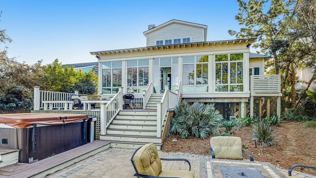 Una casa de dos pisos con un porche cubierto, mobiliario exterior y un jacuzzi.