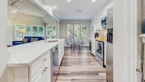 A modern kitchen with a central island, white cabinetry, and a dining area with a table and chairs. - Cozy Kiawah Island villa centrally located near local attractions (Kiawah Island)