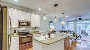 A modern kitchen with white cabinetry, a granite countertop, stainless steel appliances, and pendant lighting. - Beachy, three-story villa w/ deck & shared pool - walk downtown & to the beach (Folly Beach)