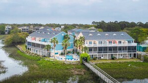A beachfront hotel with multiple balconies, a swimming pool, and a boardwalk leading to the water. - Beachy, three-story villa w/ deck & shared pool - walk downtown & to the beach (Folly Beach)