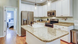 A kitchen with white cabinets, granite countertops, stainless steel appliances, and pendant lighting. - Beachy, three-story villa w/ deck & shared pool - walk downtown & to the beach (Folly Beach)
