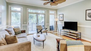 A spacious living room with a sofa, armchair, coffee table, and a TV on a stand. - Beachy, three-story villa w/ deck & shared pool - walk downtown & to the beach (Folly Beach)