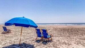 A beach with two blue beach chairs and a blue umbrella. - Exquisitely Furnished Home Surrounded by Golf Courses, Tennis Courts, & Beaches (Kiawah Island)