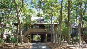 A wooden cabin with a covered walkway and a dirt path leading to it, surrounded by trees. - Exquisitely Furnished Home Surrounded by Golf Courses, Tennis Courts, & Beaches (Kiawah Island)