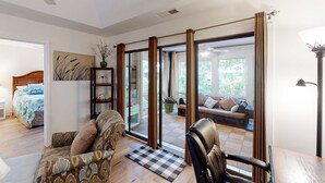 A spacious living area with a sofa, armchair, and a view through a sliding glass door to an outdoor seating area. - Exquisitely Furnished Home Surrounded by Golf Courses, Tennis Courts, & Beaches (Kiawah Island)
