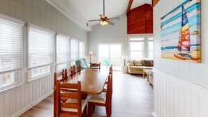 Uma área de refeições com mesa e cadeiras de madeira, ventilador de teto e uma janela grande com persianas.