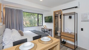 A modern hotel room with a bed, a dining table with plates, a TV, and an air conditioning unit. - Edificio Bloom (Medellín)