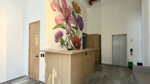 A reception area with a wooden reception desk, a wall mural of flowers, an elevator, and a grey door. - Edificio Bloom (Medellín)